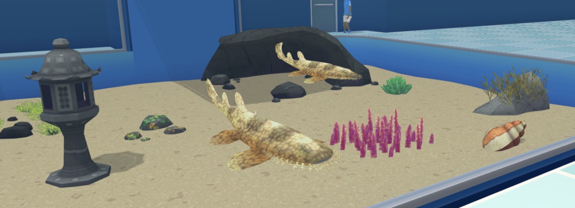 Twee Franjebakerhaaien (één op de voorgrond, één achteraan voor een Gaping Cavern) in hun Aquarium. De Vissen zijn langwerpig en hebben een bruingele, gestippelde camouflagekleur. 'Franjes' op de mond dragen bij aan de camouflage. In het Aquarium liggen ook nog een Lantaarn, een Slakkenschelp en diverse Planten en Rotsen.