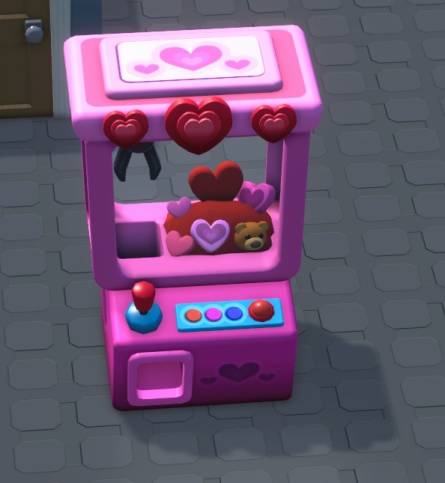 Vogelperspectief van een Claw-at-Love-automaat: een klassieke automaat-met-grijpkraan, maar dan in knalroze, met hartvormige speeltjes als prijs. Vooraan zit links de joystick en rechts drie kleine en één grote drukknop. Bovenaan staan drie rode hartjes gemonteerd; op het 'dak' staan eveneens drie hartjes getekend en aan de voorkant staan rechts twee kleine hartjes, met daartussen één groter hart. Links vooraan zit de uitneembak.