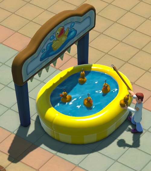 Vogelperspectief van een Hook-a-Duck Game: een geel, gevuld opblaaszwembad waarin vier enorme plastic eendjes drijven. Rechts heeft een Dokter-Student net een eendje gevangen. Achter het 'zwembad' staat een houten bord met een lachend eendje in het midden. Onder het bord hangen driehoekige vlaggetjes.