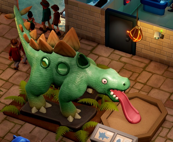 Een enorm speeltuig in de vorm van een Stegosaurus, met een tong als glijbaan. Rechtsboven overziet een Veiligheidscamera de omgeving.