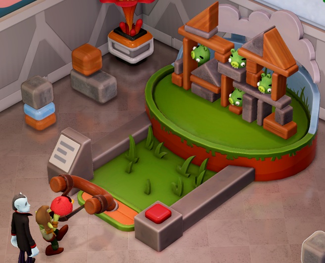 Een installatie met achteraan een 'fort' opgebouwd uit (bouw)blokken en 'Bad Piggies'. Aan de voorkant zit een enorme katapult, waarmee projectielen in de vorm van 'Red' op het 'fort' worden afgeschoten. Een Dwerg spant net de katapult op, terwijl een Vampier achter hem zijn beurt afwacht.